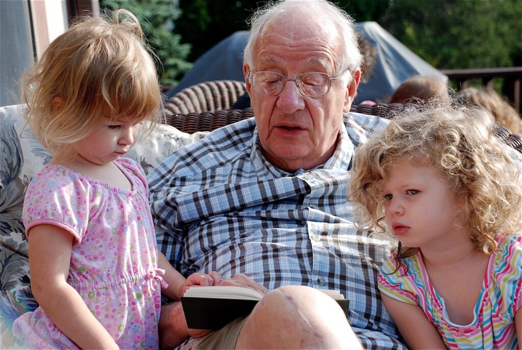 Ted Loder reading a book to Hannah (3), who is looking skeptical and Chloe (4), who is imagining the story.