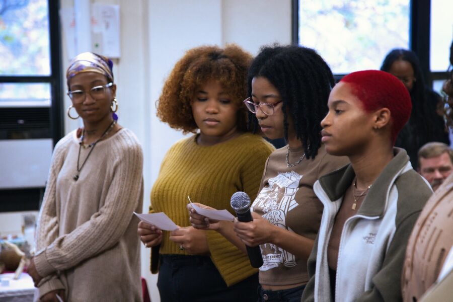 African and African American Studies students standing in a row, from left to right: Amber McAddley, Morgan Braswell, Jhala Martin, and Ayodele Uhuru. They are listening to Jhala read from a piece of paper with a microphone in her hand. Photo by Ryan Frederick.