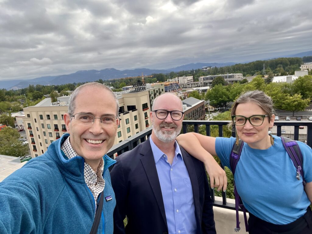 A selfie with Chris Long, Jason Rhody, and Nicky Agate on the roof of the Graduate Hotel in Eugene with Autzen Stadium and mountains in the background.