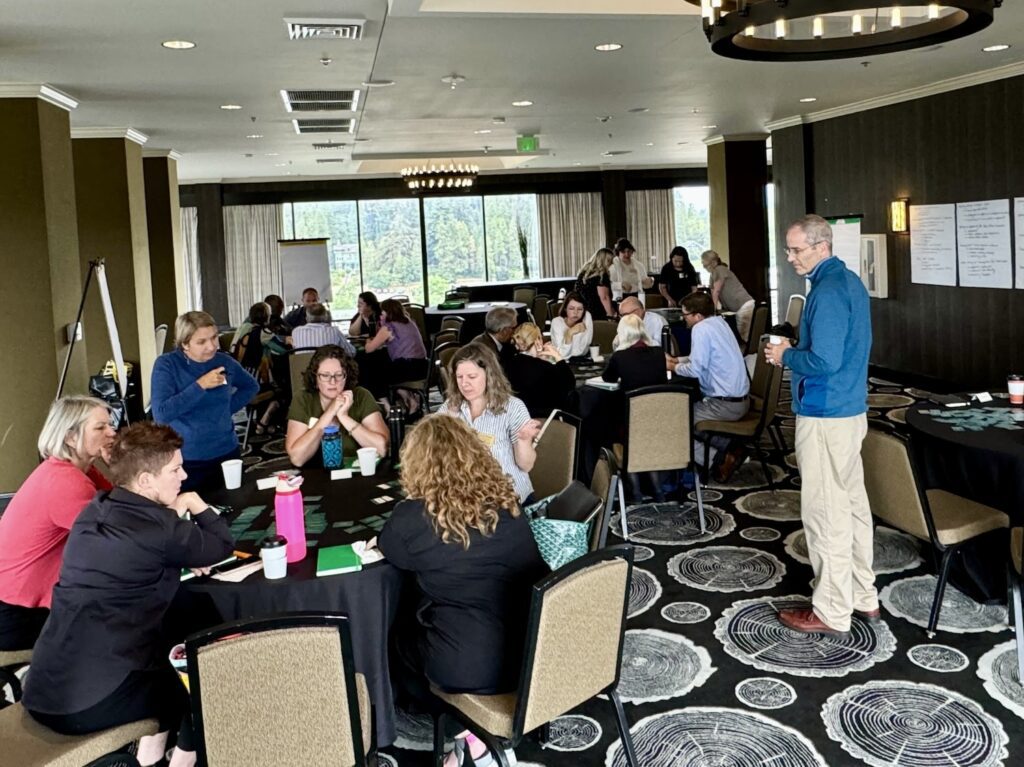 A room with groups of people working on values frameworks at the Office of the Provost Retreat. Provost Long looks on as values are being shared and identified.